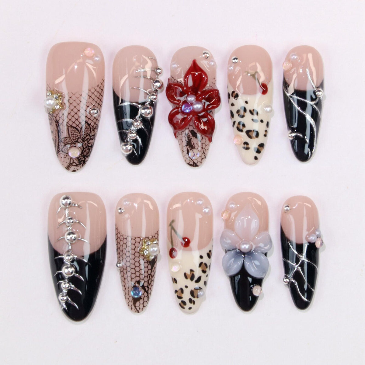 A set of ten almond-shaped artificial nails. Designs include black and nude bases with lace, floral, and animal print accents. Embellishments include rhinestones and pearls. Some nails feature a black French tip.