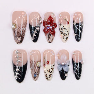 A set of ten almond-shaped artificial nails. Designs include black and nude bases with lace, floral, and animal print accents. Embellishments include rhinestones and pearls. Some nails feature a black French tip.