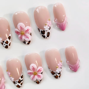 Set of artificial nails with a nude base, featuring various designs. Some nails have a leopard print tip, others have 3D pink flower accents with gold centers, and some have a pink and clear design.