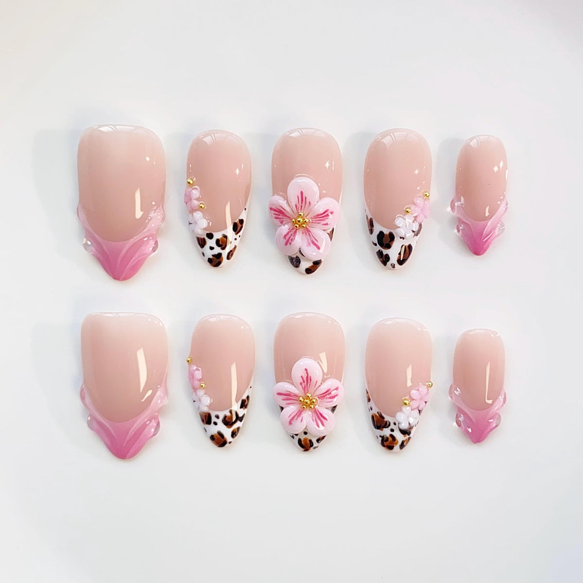 A set of ten artificial nails in various shapes. The nails feature a nude base with a pink French tip, leopard print accents, and 3D flower embellishments. Some nails have a pink floral design.