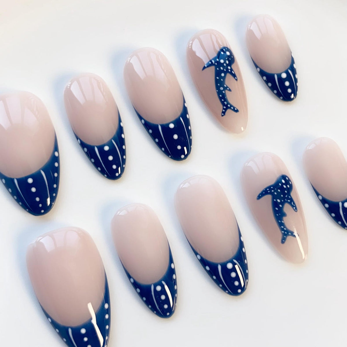 Oval-shaped false nails with a light pink base and a navy blue French tip with white polka dots. Some nails feature a navy blue whale shark design with white polka dots.