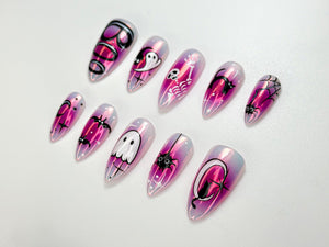 A set of ten iridescent, almond-shaped false nails. Each nail features a different Halloween-themed design in black and white, including ghosts, bats, spiders, and skeletons, set against a pink and purple gradient.