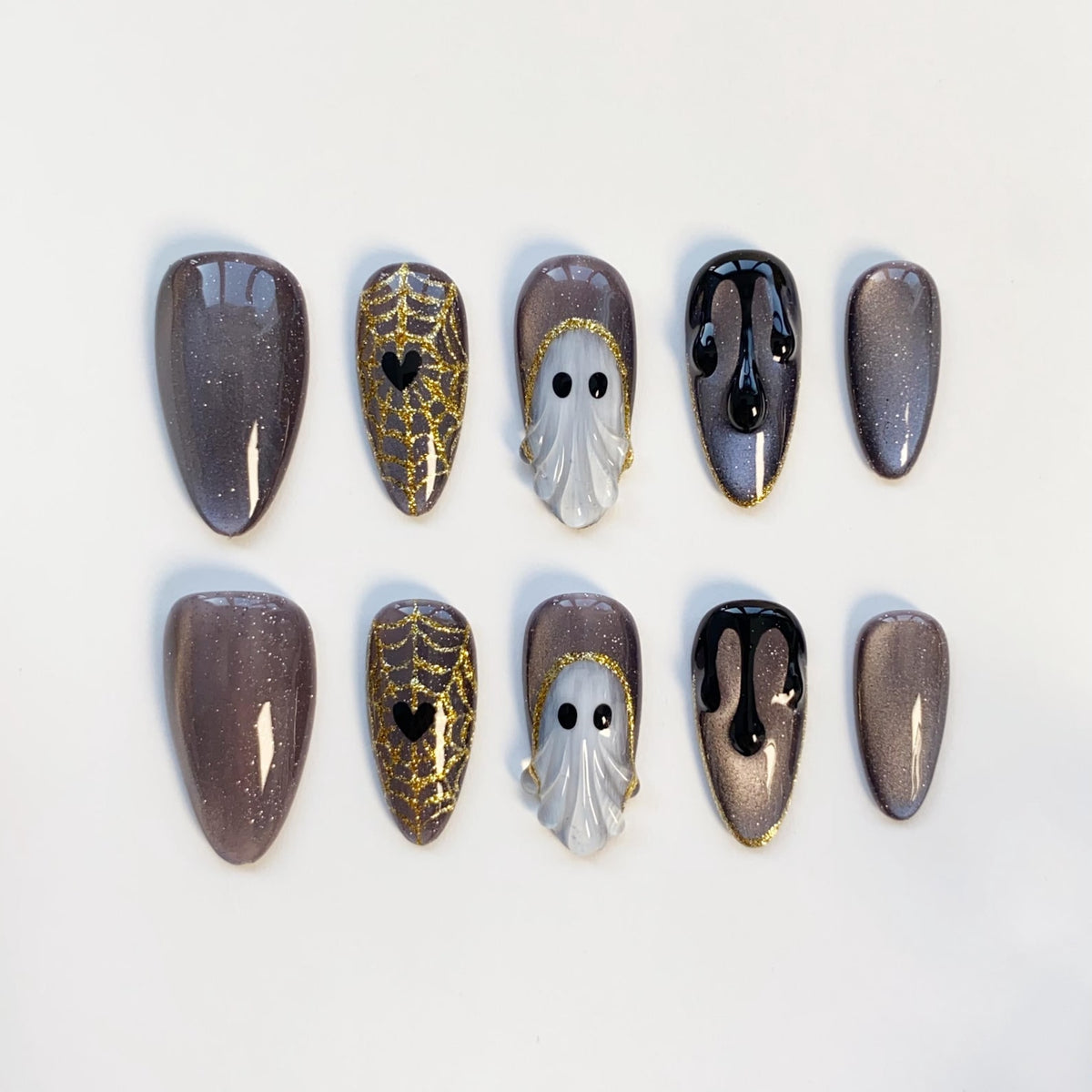 A set of ten Halloween-themed false nails. Designs include glittery gray, gold spiderwebs with black hearts, white ghost figures, and black dripping paint. The nails are almond-shaped and arranged on a white surface.