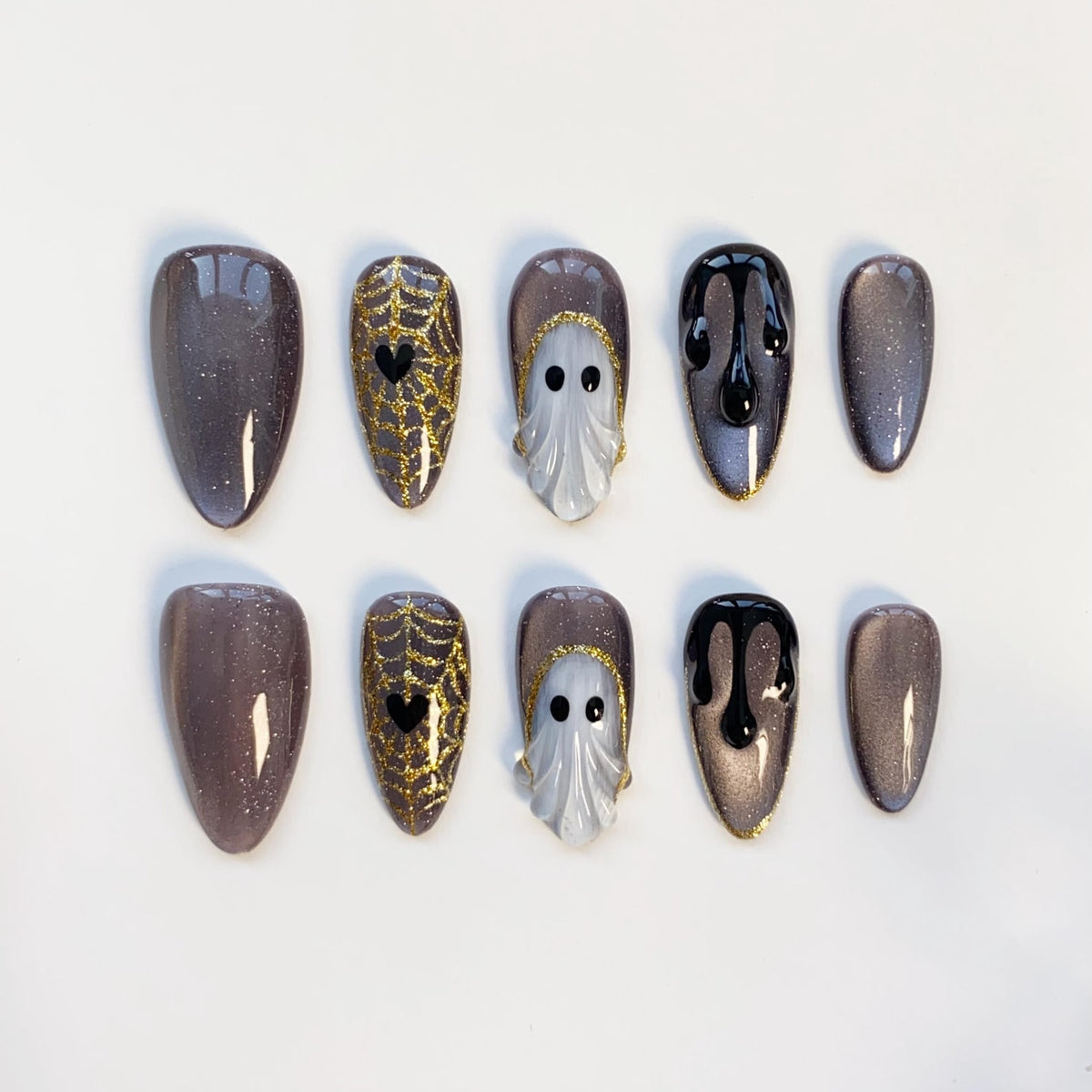 A set of ten press-on nails in various designs. Some nails are a shimmery gray, others feature gold spiderwebs with black hearts, white ghost designs, and black dripping paint. The nails are oval-shaped.