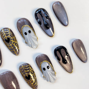 A collection of Halloween-themed nail art designs. The nails feature a variety of designs, including a ghost, spiderwebs with hearts, and dripping black polish. The nails are primarily shades of gray, black, and gold.