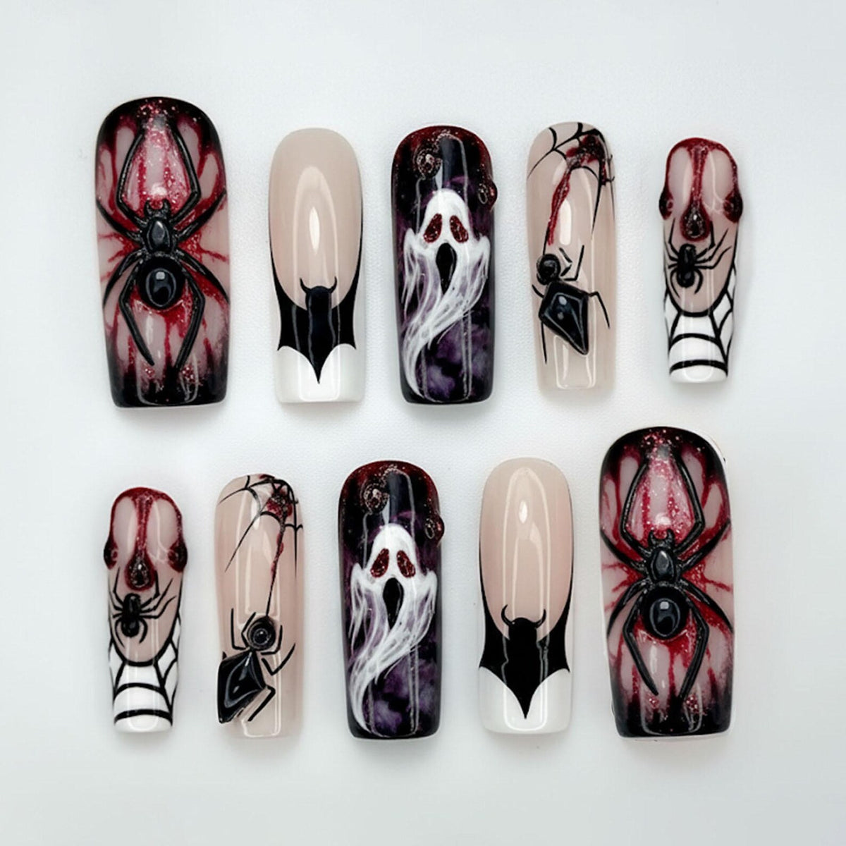 A set of ten Halloween-themed false nails. Designs include spiders, spiderwebs, and ghosts, with a color palette of black, red, white, and nude. The nails are rectangular and have a glossy finish.