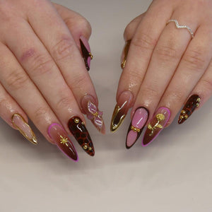 Long, almond-shaped nails with a variety of designs. Some nails feature a gradient of pink and brown, others have gold accents, and some have a leopard print pattern. Gold embellishments and a gold ring are also visible.