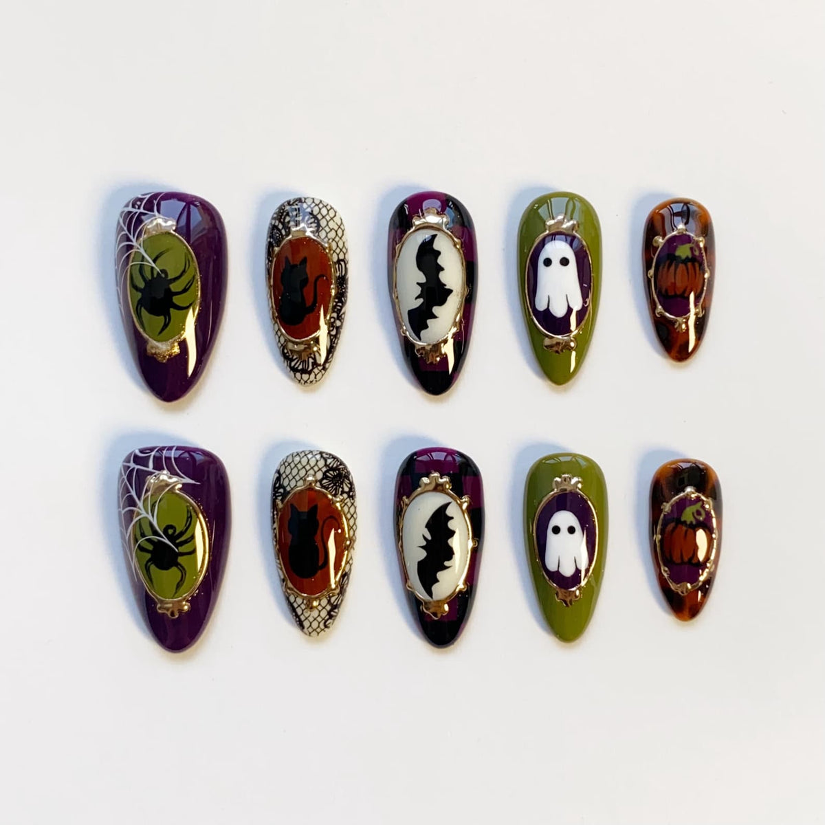 A set of ten Halloween-themed press-on nails. Each nail features a different design, including a spider and web, a black cat, a bat, a ghost, and a pumpkin. The nails are oval-shaped and painted in various colors, including purple, green, and orange.