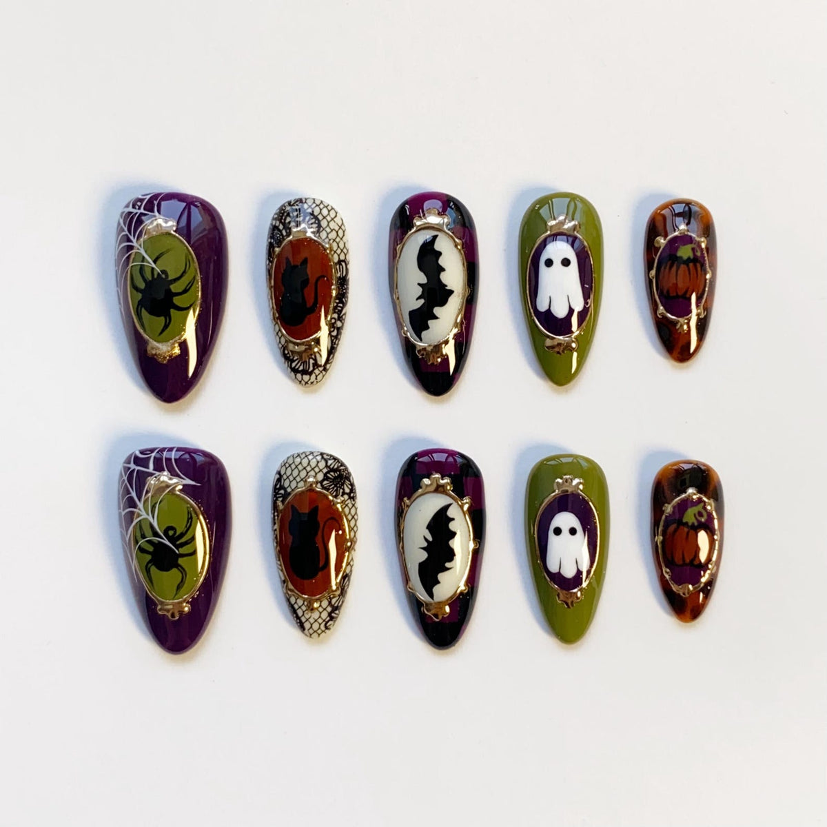 A set of ten Halloween-themed press-on nails. Each nail features a different design, including a spider and web, a black cat, a bat, a ghost, and a pumpkin. The nails are oval-shaped and painted in various colors, including purple, green, and orange.
