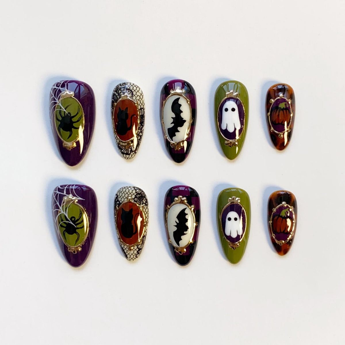A set of ten press-on nails with Halloween-themed designs. Each nail features a different design, including a spider, cat, bat, ghost, and pumpkin. The nails are oval-shaped and painted in various colors, including purple, green, and orange.
