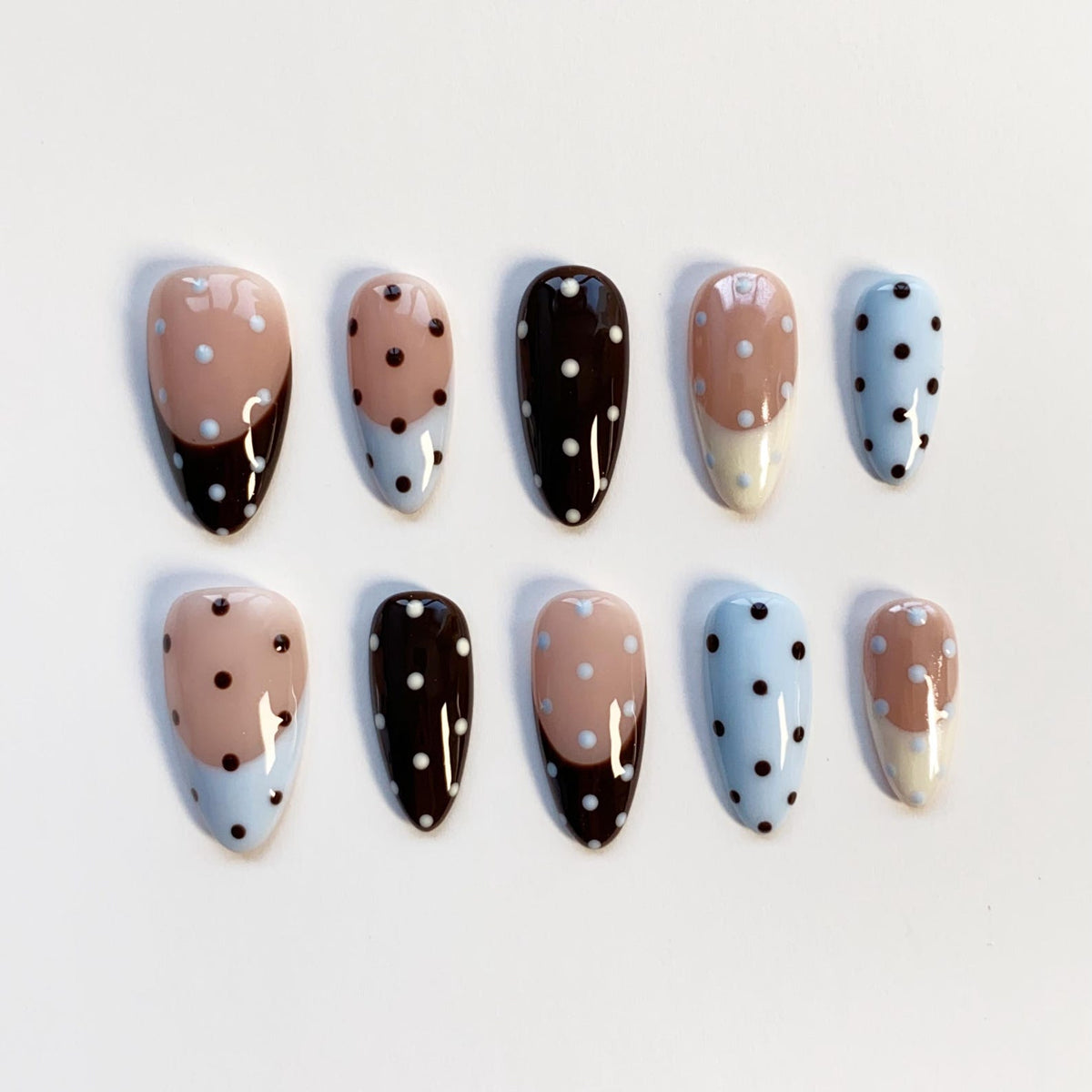 A set of ten oval-shaped false nails. The nails feature a variety of designs, including solid colors, polka dots, and color-blocked patterns. Colors include light blue, brown, and beige.