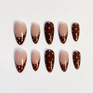 A set of ten almond-shaped false nails. The nails feature a light beige base with a dark brown French tip adorned with small white polka dots. The design is consistent across all nails, offering a cohesive look.