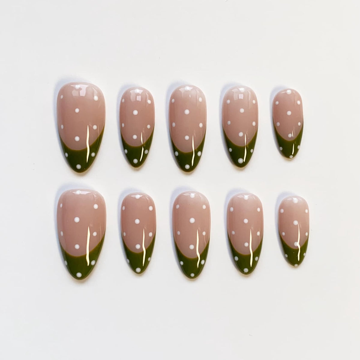 Set of ten almond-shaped false nails. Each nail features a nude base with white polka dots and a dark green French tip. The nails are arranged on a white surface.