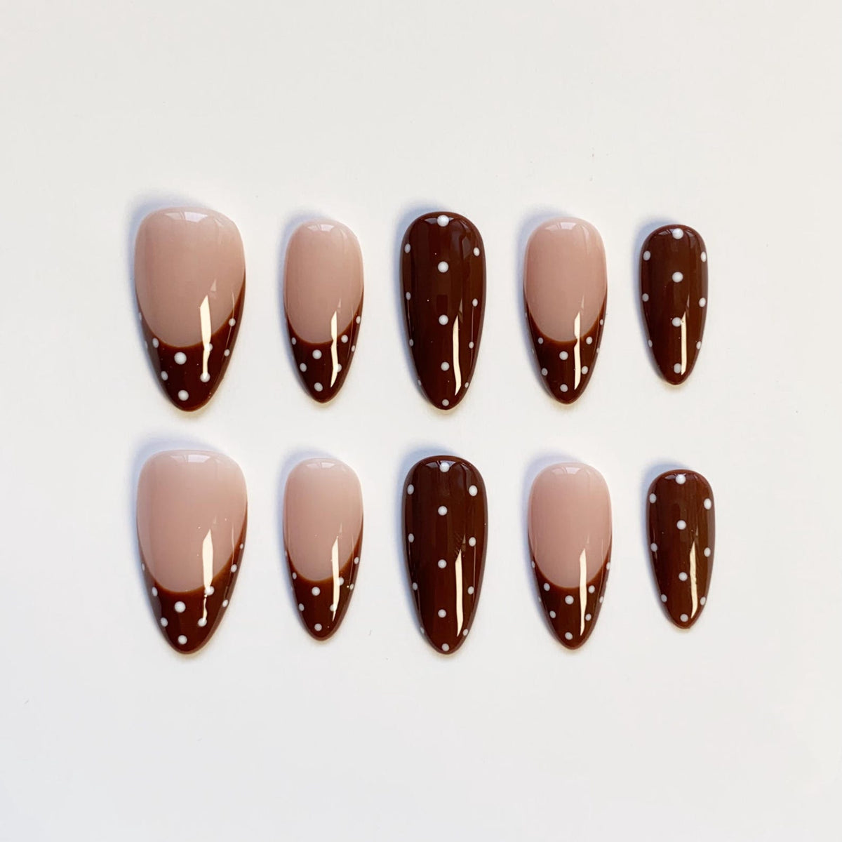 Set of ten almond-shaped false nails. Each nail features a nude base with a dark brown tip, accented with white polka dots. The nails are arranged on a white surface.
