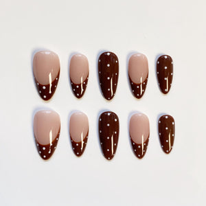 Set of ten almond-shaped false nails. Each nail features a nude base with a dark brown tip, accented with white polka dots. The nails are arranged on a white surface.