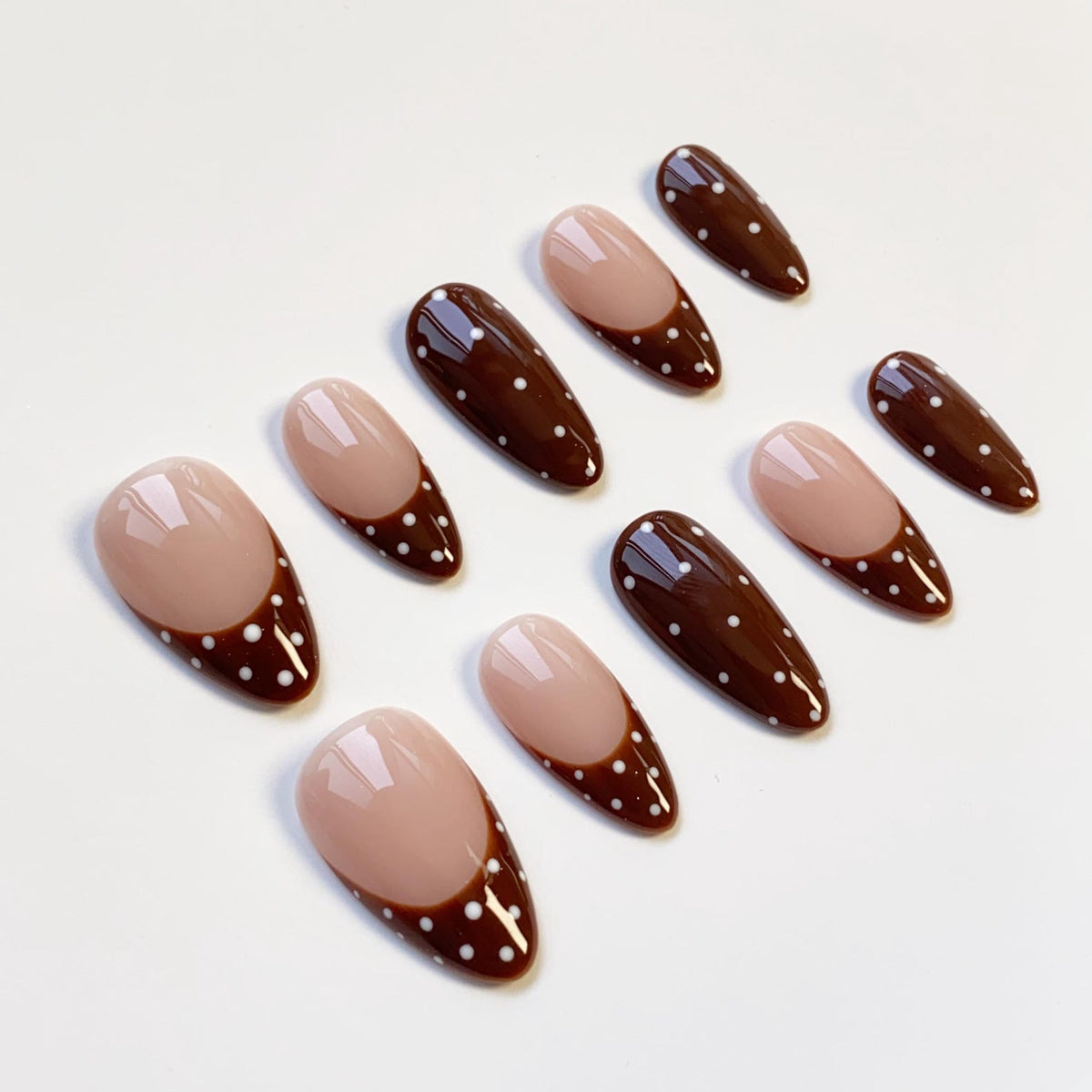 Set of ten almond-shaped false nails. Each nail features a light brown base with a dark brown tip adorned with white polka dots. The nails are arranged on a white surface.