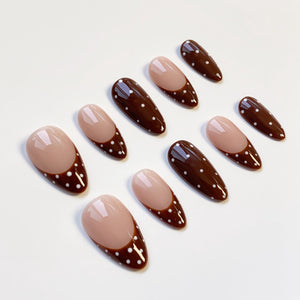Set of ten almond-shaped false nails. Each nail features a light brown base with a dark brown tip adorned with white polka dots. The nails are arranged on a white surface.
