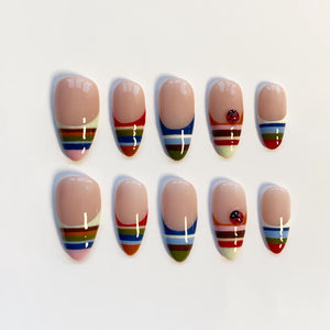 Set of ten artificial nails with a nude base and colorful striped designs. Some nails feature a small ladybug accent. The nails are oval-shaped and have a glossy finish, perfect for a manicure.