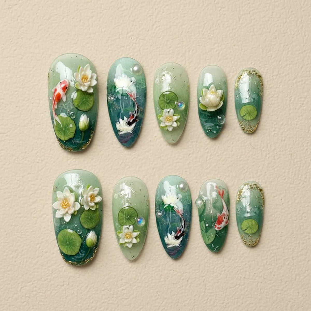 A set of ten almond-shaped artificial nails with a water lily and koi fish design. The nails feature a gradient of green and blue hues, with 3D floral and fish accents. The design includes water lilies, lily pads, and koi fish.