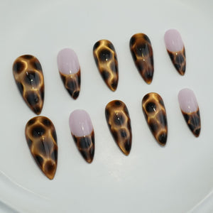 Set of ten almond-shaped false nails. The nails feature a glossy, tortoiseshell pattern in shades of brown and black. Some nails have a light pink tip with a brown accent.