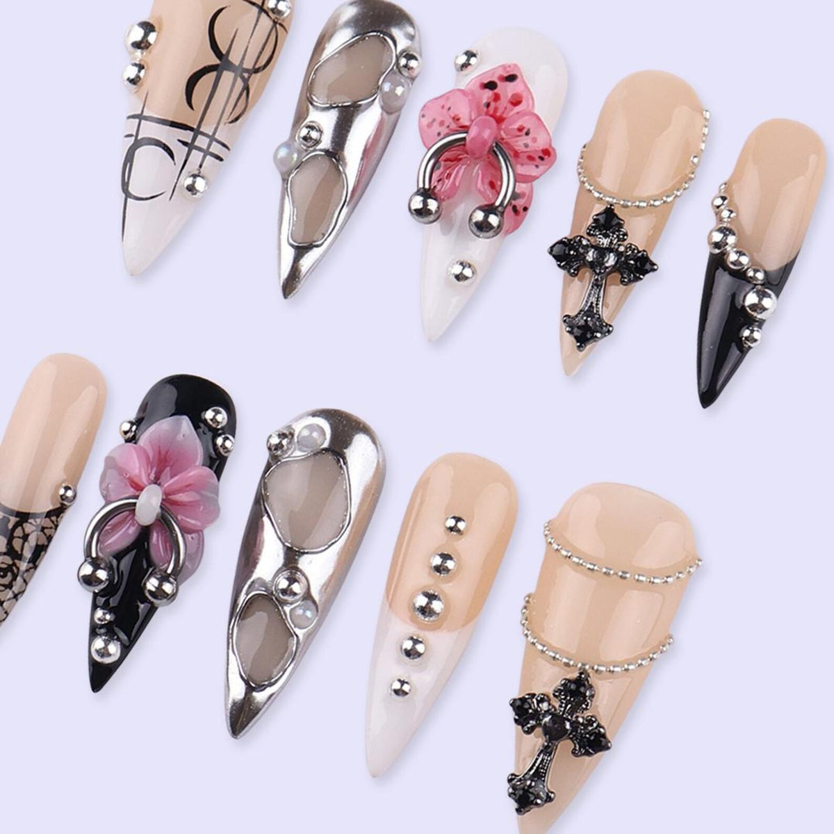 A collection of artificial nails in various designs. Some nails are nude, black, or white, adorned with silver embellishments, floral accents, and cross pendants. The nails have a pointed shape.