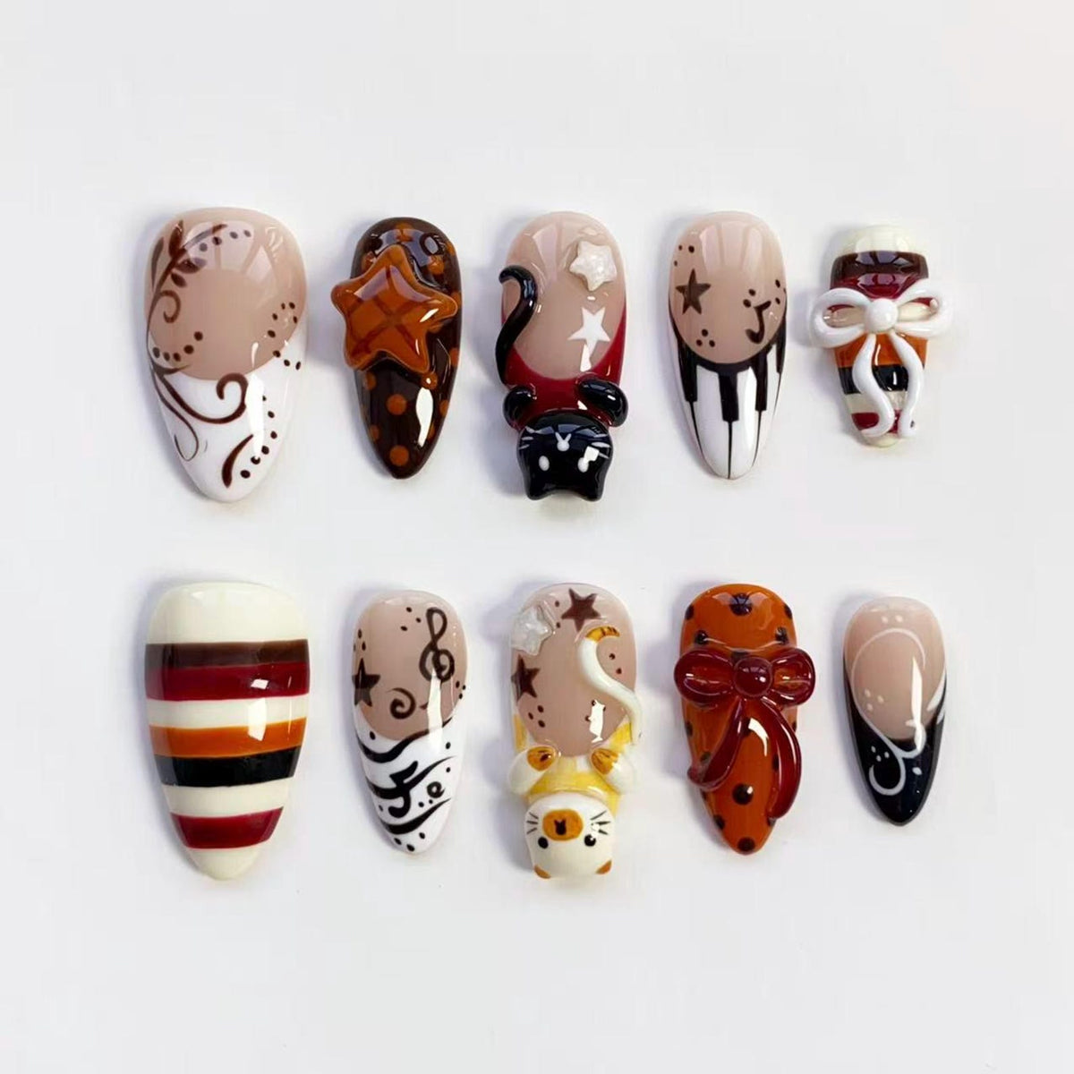 A collection of ten artificial nails with various designs. The nails feature a range of colors, including beige, brown, red, and white, with decorative elements such as stars, musical notes, and bows. Some nails have 3D embellishments.