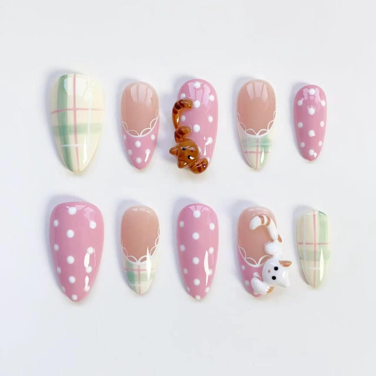 A set of ten artificial nails in various designs. Some nails are pink with white polka dots, others are a light peach color with a white lace design. Two nails feature 3D cat and bear charms, and two have a plaid pattern.