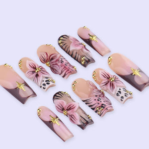 A set of ten artificial nails with a floral design. The nails feature a gradient of light pink to brown, with gold star and bead accents. The floral design includes pink flowers and black and white leopard print.