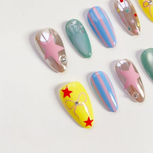 A collection of artificial nails in various designs. Some nails are clear with pink star accents, others are teal with glitter, and some feature blue and pink stripes. One nail is yellow with red stars and a bow.