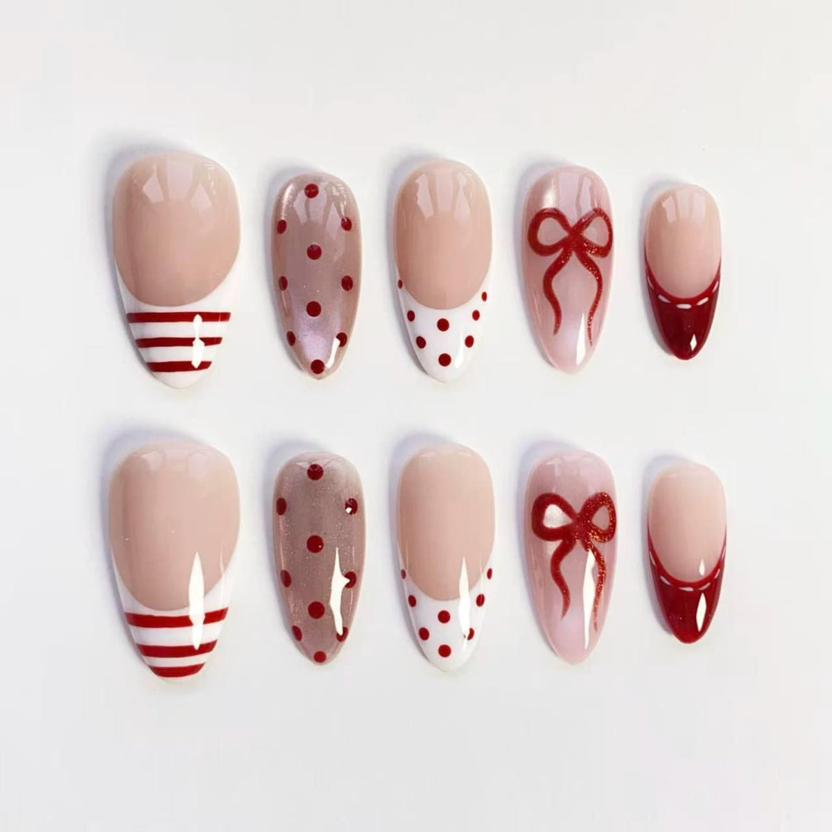 A set of ten artificial nails in various designs. The nails feature a nude base with red stripes, polka dots, bows, and French tips. The nails are oval-shaped and arranged on a white surface.