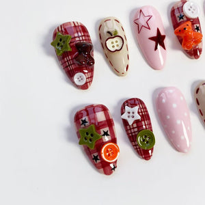 A collection of decorated fingernails. Designs include red plaid, pink with white polka dots, and beige with an apple design. Embellishments include star-shaped buttons, teddy bears, and other decorative elements.