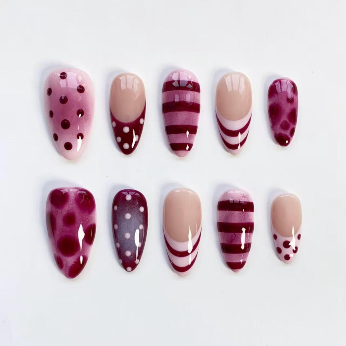 A set of ten artificial nails in various designs. The nails feature patterns such as polka dots, stripes, and a speckled design. Colors include shades of pink, burgundy, and nude.