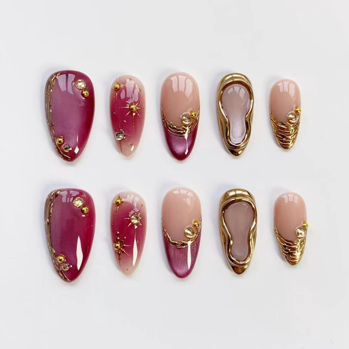 A set of ten artificial nails in various designs. Some nails are a deep burgundy with gold accents, while others are a nude pink with gold embellishments. One design features a gold frame.