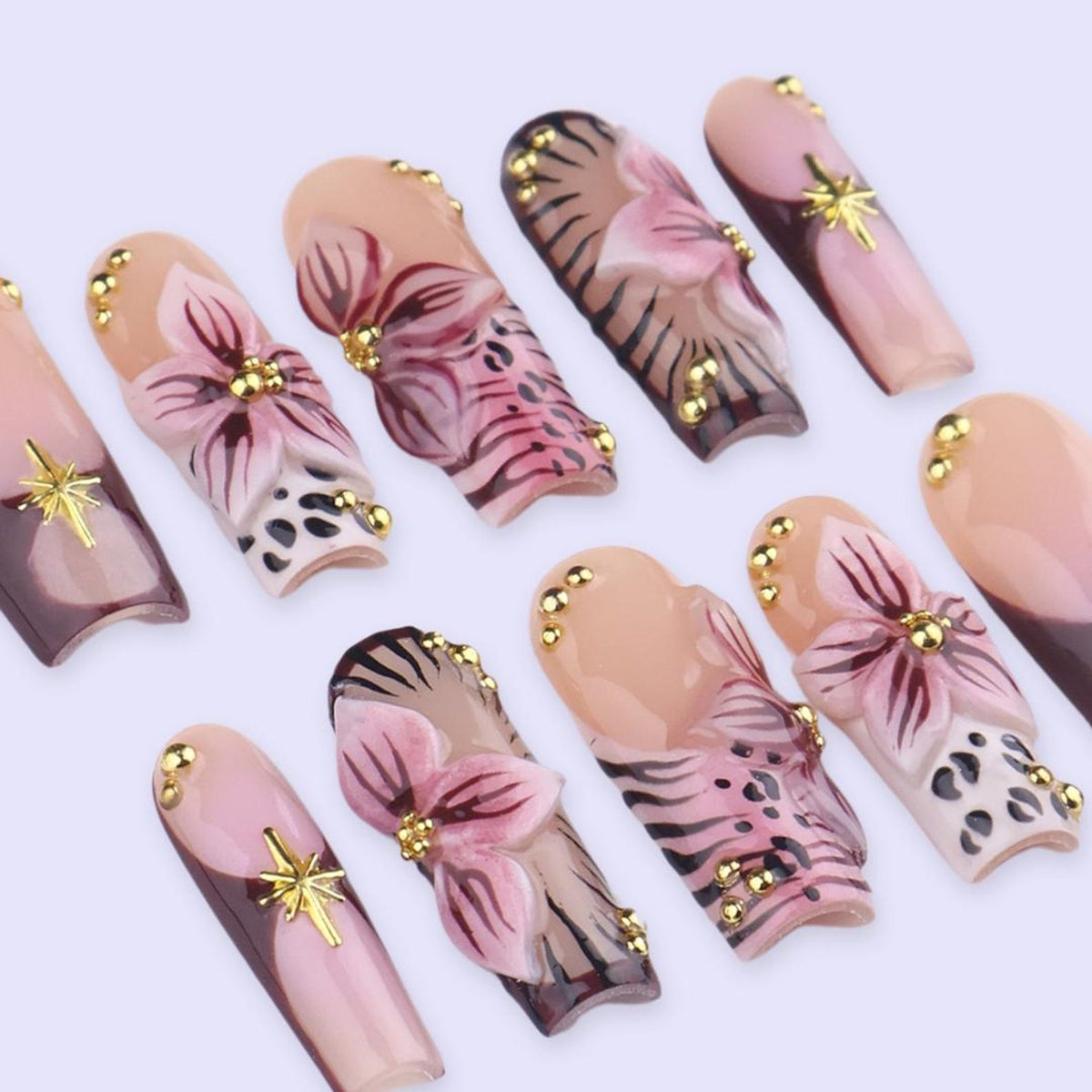 A collection of artificial nails with floral and abstract designs. The nails feature a variety of colors, including pink, brown, and gold. Some nails have a flower design, while others have a leopard print or gold accents.
