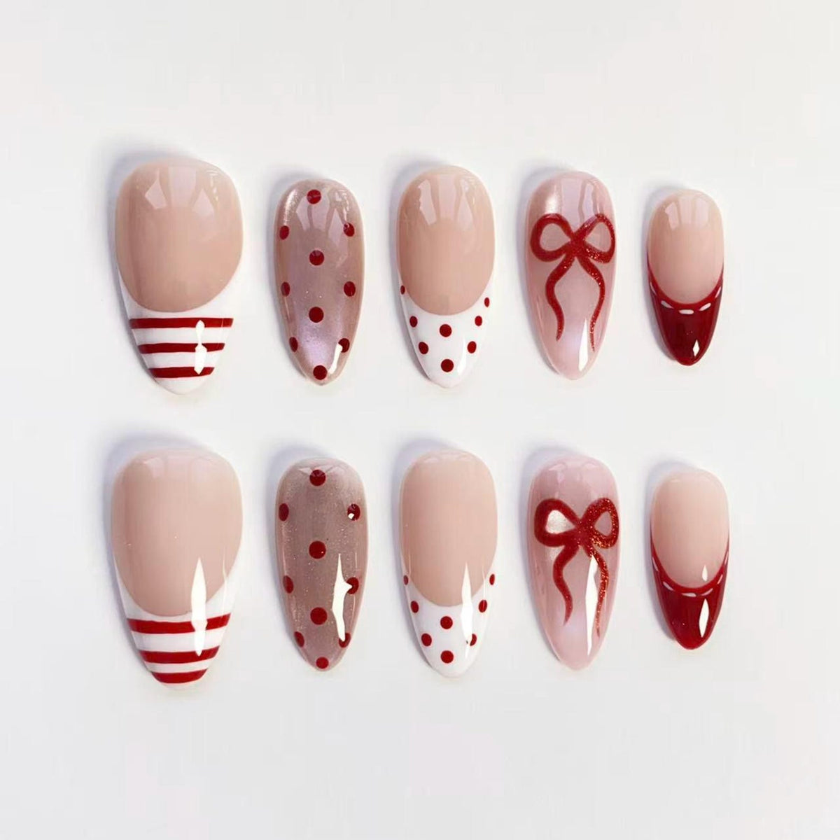 A set of ten artificial nails with various designs. The nails feature a nude base with red accents, including stripes, polka dots, bows, and French tips. The nails are oval-shaped and arranged on a white surface.