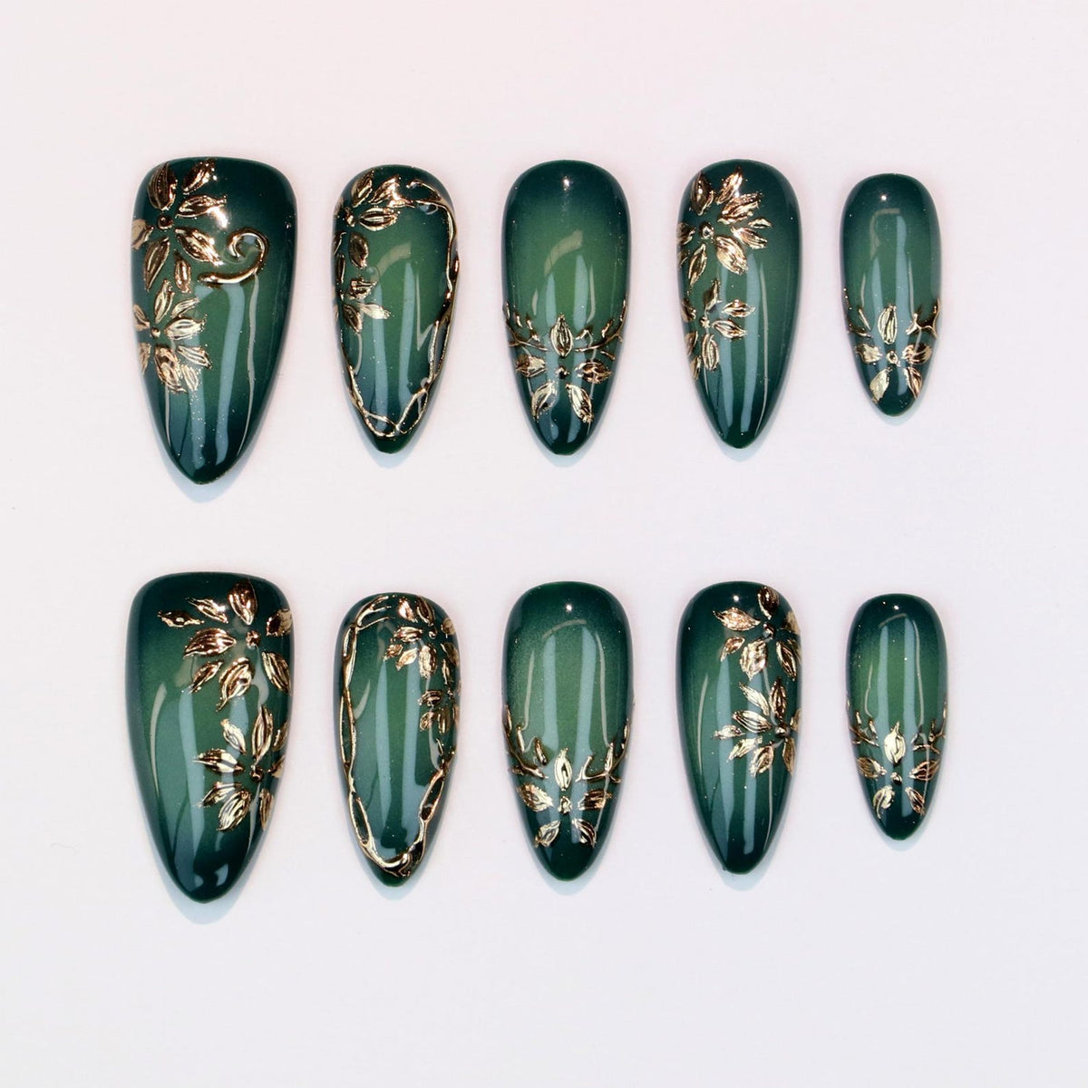 Set of ten almond-shaped, press-on nails. Each nail is a deep teal green with a gold floral design. The gold accents vary in style, with some featuring full floral patterns and others with delicate outlines.