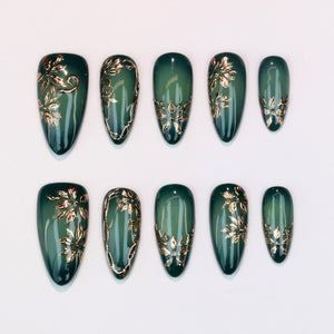 Set of ten artificial nails in various sizes. Each nail is a deep green color with a gold floral design. The nails have an oval shape and a glossy finish, perfect for a manicure.