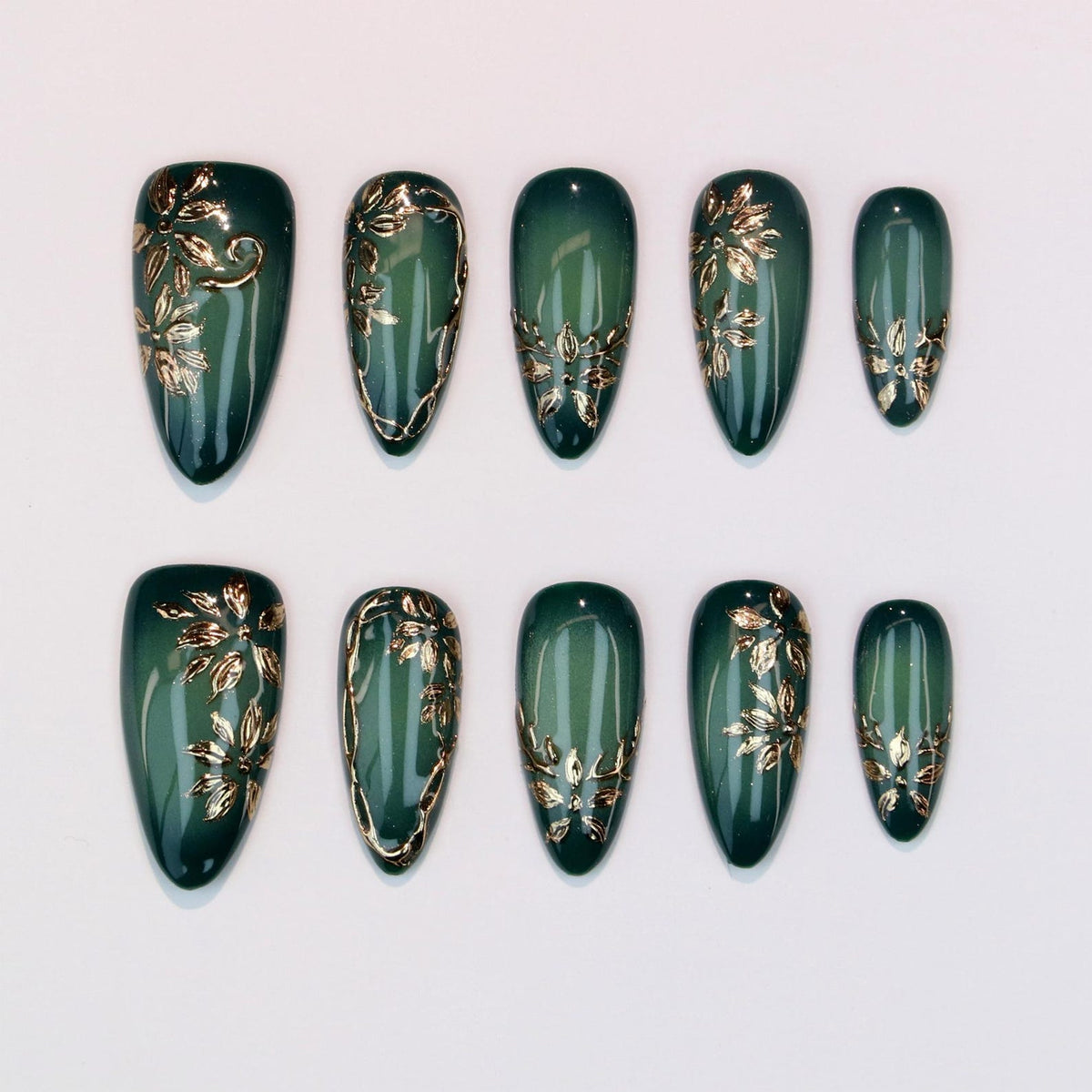 Set of ten emerald green press-on nails with gold floral designs. The nails are oval-shaped and feature varying gold leaf and vine patterns. The nails are arranged on a white surface.