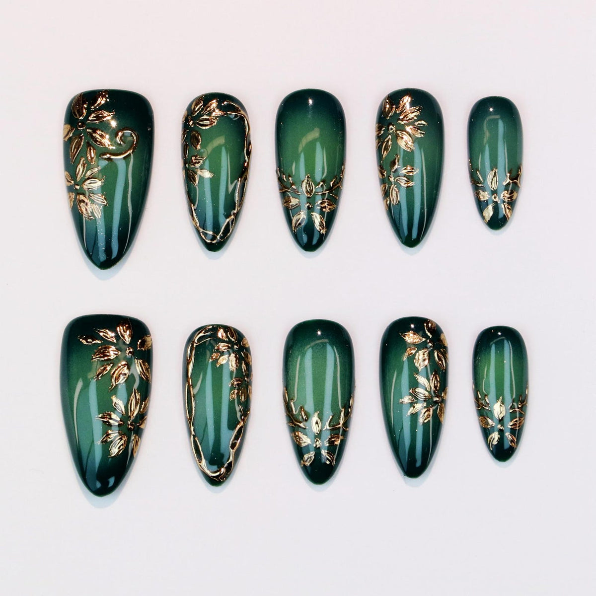Set of ten emerald green press-on nails with gold floral designs. The nails are oval-shaped and feature a glossy finish. The gold accents are applied in various floral patterns, adding a touch of elegance.