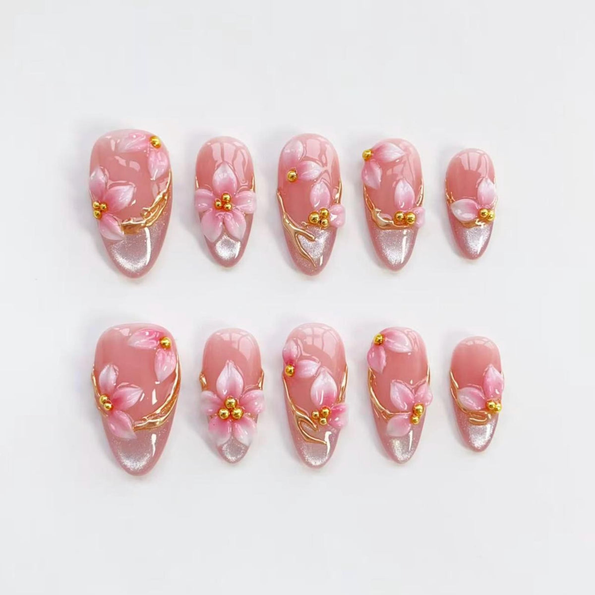 A set of ten artificial nails in various sizes. Each nail is oval-shaped and features a pink base with a floral design. The flowers are pink with gold accents, and the nails have a gold swirl design.