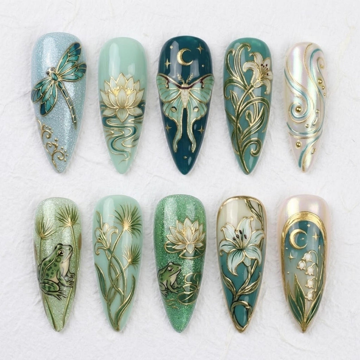 A set of ten long, almond-shaped artificial nails with intricate designs. The nails feature detailed artwork of dragonflies, moths, flowers, and frogs in shades of blue, green, and gold. The designs are embellished with glitter and metallic accents.