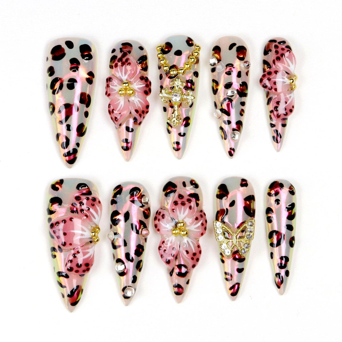 A set of ten long, pointed artificial nails. Each nail features a leopard print design in shades of pink and brown. Some nails are adorned with 3D floral embellishments, rhinestones, and gold-colored charms.