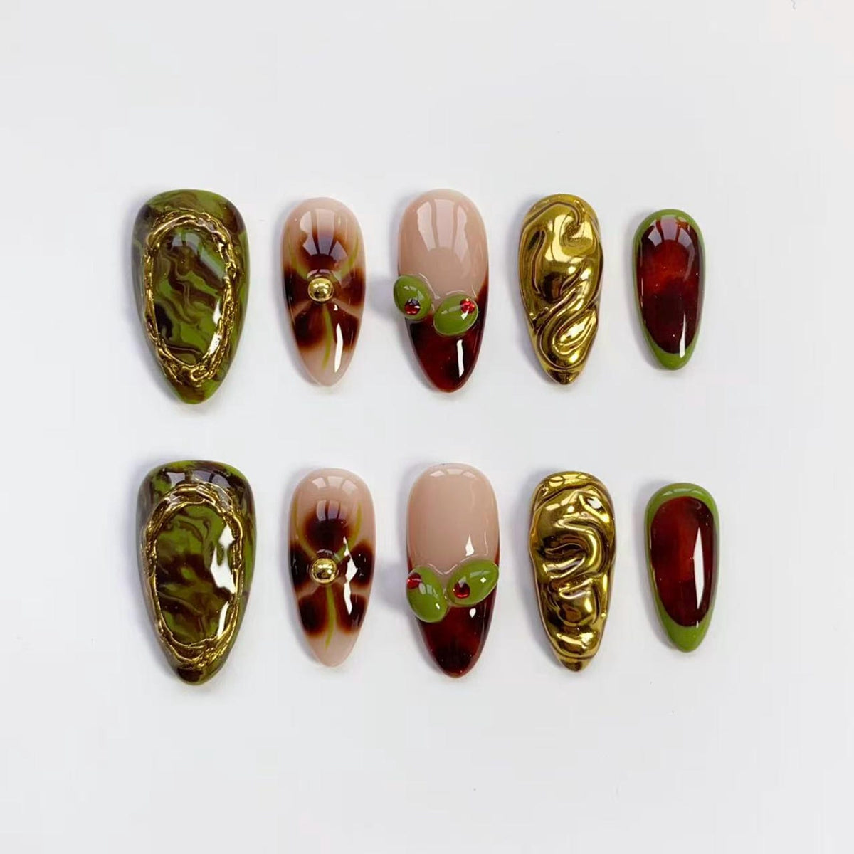 A set of ten artificial nails in various designs. Some nails feature a gold swirl design, others have olive and red accents, and some have a gold border with a green and brown marbled effect. The nails are oval-shaped.