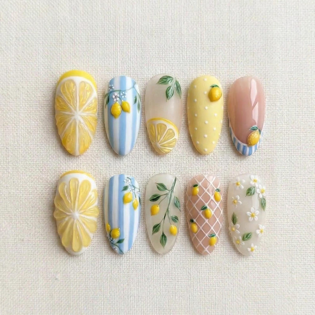 A set of ten almond-shaped artificial nails with various lemon-themed designs. The designs include lemon slices, polka dots, stripes, and floral patterns, all in yellow, white, and blue colors.