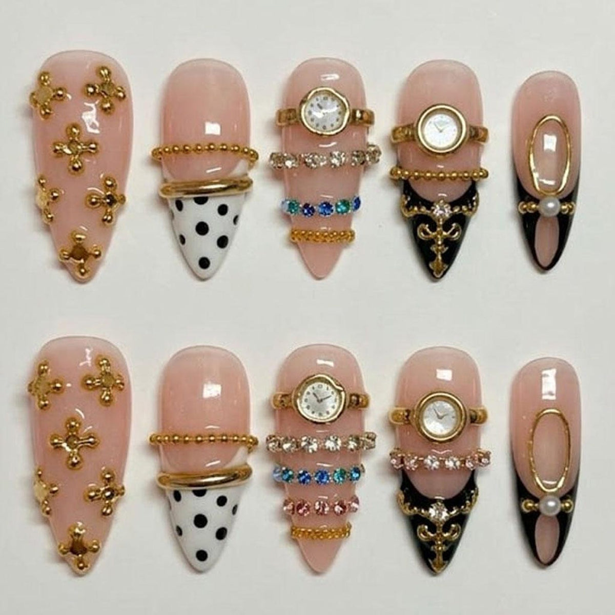 A set of ten artificial nails in various designs. Some nails are light pink with gold embellishments, while others feature watch faces, rhinestones, and black and white polka dots. The nails are almond-shaped.