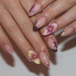 A close-up of a hand with long, almond-shaped nails. Each nail features a unique design, including floral patterns, polka dots, and gold accents. The color palette includes pink, white, burgundy, and gold, creating a feminine and artistic aesthetic.