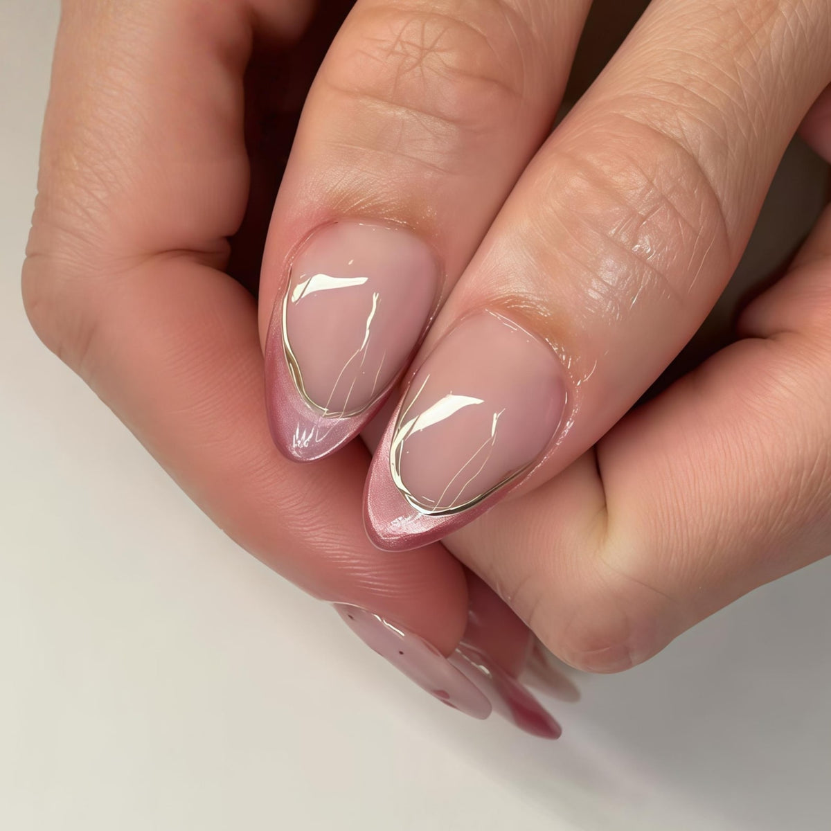 Close-up of manicured nails with a soft pink base and a silver metallic outline. The nails have a rounded shape and a glossy finish. Delicate silver lines extend from the outline, adding a touch of elegance to the design.