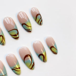 Oval-shaped false nails with a light pink base, transitioning to a light blue and yellow gradient. A dark brown, curved design adorns each nail. The nails are arranged on a white surface.