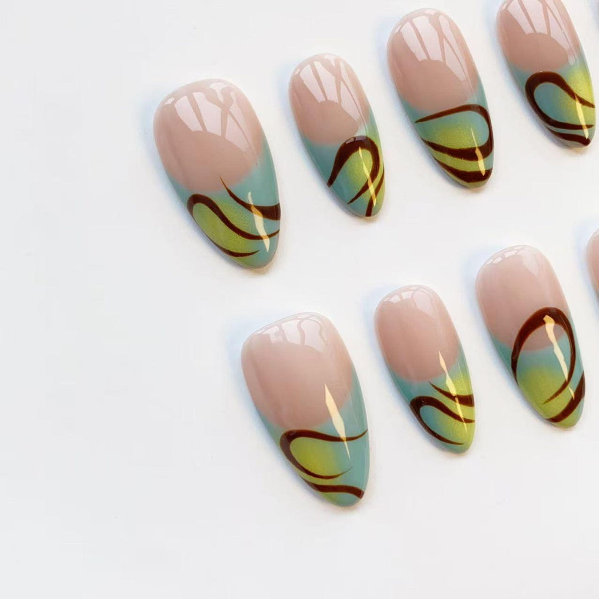 Oval-shaped false nails with a nude base, a light blue tip, and a brown and yellow swirl design. The nails are arranged on a white surface, showcasing a modern and artistic nail art style.