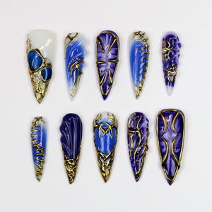 A collection of ten long, almond-shaped artificial nails. Each nail features a unique design with shades of blue, white, and gold. The designs include swirls, geometric patterns, and ornate gold accents, creating a luxurious and artistic aesthetic.